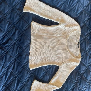 Lätt och luftig, vit stickad tröja med vida armar - Säljer en stilren och trendig stickad cropp tröja, använd bara några gånger, sitter inte som ett XL plagg. Den har en vid rund hals och lätt utsvängda armar. Passformen är något kroppsnära men stretchiga och bekväm att bära💕
