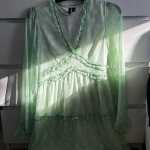 Grön klänning från Vero Moda - Säljer en söt ljusgrön klänning från Vero Moda med volangdetaljer och v-ringning. Klänningen har långa, transparenta ärmar och ett fint fall. Perfekt för vår och sommar! Hör av dig vid intresse🤗