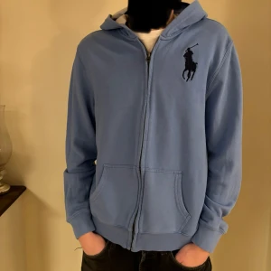 Polo Ralph Lauren Zip - Säljer en snygg blå hoodie från Ralph Lauren med dragkedja och det klassiska logotypbroderiet på bröstet. Tröjan har långa ärmar och en bekväm passform med fickor framtill. Perfekt för en avslappnad stil. Nypris på denna är 1999. Hör av er vid några frågor. Pris kan diskuteras 