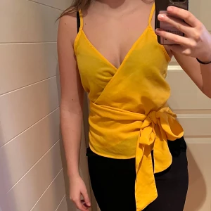 Gul omlottopp från Bik Bok - Säljer en snygg gul omlottopp från Bik Bok med smala axelband och knytning i midjan.