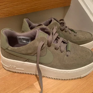 Nike Air Force 1 i fin grön mocka/skinn  storlek 38 1/2 - Snygga Nike Air Force sneakers i en fin grön färg.  Skorna har en klassisk design med snörning och en bekväm sula. Perfekta för en avslappnad stil. Skicket är väldigt bra endast använda vid 2 tillfällen. 