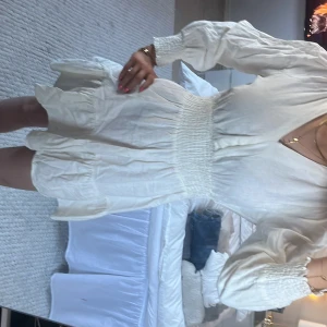 Vit klänning med v-ringning - Säljer en söt vit klänning med v-ringning och långa ärmar. Klänningen har en smockad midja och volangdetaljer vid fållen. Som ni ser på sista bilden är den lite ”trasig” men annars jätte fin! Skriv vid frågor och funderingar!💕