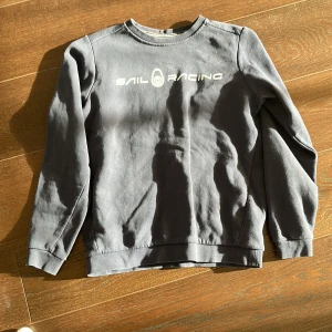 Blå sweatshirt från Sail Racing - Säljer en stilren blå sweatshirt från Sail Racing med tryckt logga på bröstet. Tröjan har rund hals och långa ärmar, perfekt för en avslappnad stil. Passar bra till jeans. Storlek 160. Bra skick 