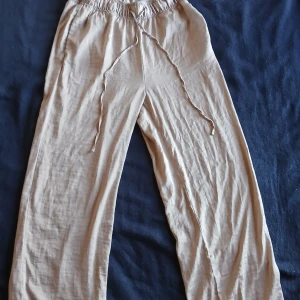 Beige linne byxor från H&M - Säljer ett par bekväma beige byxor från H&M. De har en loose passform med elastisk midja och snörning för justering. Perfekta för sommaren har en liten vit fläck vid vänstra fickan 