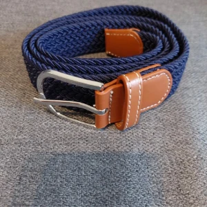 Blått flätat bälte med bruna detaljer - Snyggt flätat bälte i blått med bruna läderdetaljer och ett stilrent silverfärgat spänne. Perfekt för att ge en casual look lite extra stil. Passar till både jeans och chinos.