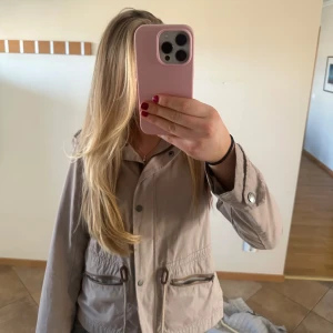 Beige kappa  - Säljer en stilren beige jacka från Barbour med knappar och dragkedja. Jackan har långa ärmar och praktiska fickor med dragkedjor. Perfekt för vår och höst! Värkligen jätte fin!!❣️❣️❣️ storlek S-M