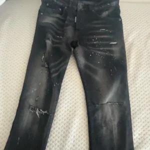 Svarta jeans med slitningar från Dsquared2 - Snygga svarta jeans från Dsquared2 med coola slitningar och färgstänk. De har en modern design med knappgylf och femficksmodell. Perfekta för en trendig look.