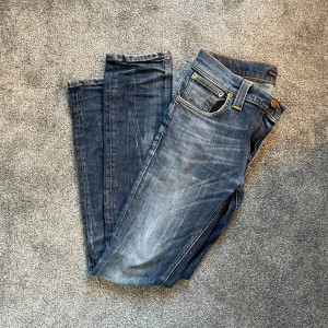 Blå jeans från Nudie Jeans - Säljer ett par snygga blå jeans från Nudie Jeans. De har en klassisk femficksdesign med en lätt slitning för en cool look. Perfekta för en avslappnad stil. Passformen är slim och de har en knappgylf.