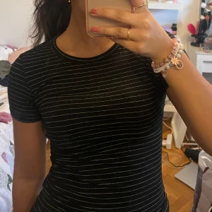 Svart och vit randig t-shirt - Säljer en svart t-shirt med vita ränder. Den har en rund halsringning och korta ärmar. Perfekt för en avslappnad stil.