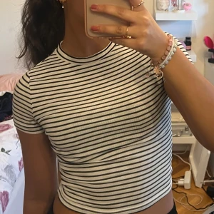 Randig kortärmad topp - Säljer en stilren randig topp i svart och vit. Den har en tight passform och korta ärmar, perfekt för en avslappnad look. Toppen är ribbad vilket ger en extra touch av textur.