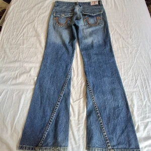 True Religion med brodyr! - Fräsha jeans från True Religion med bootcut-stil och unika bakfickor med broderade detaljer. Saknar en knapp där bak och därmed kan pris diskuteras men utöver det är jeansen i mycket bra skick! 