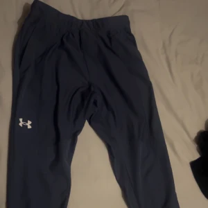 Blå träningsbyxor från Under Armour - Snygga blå träningsbyxor från Under Armour med elastisk midja och dragkedja på fickan. Perfekta för träning eller vardagligt bruk. Slutsålda på JD sports, originalpris 1100 kr 
