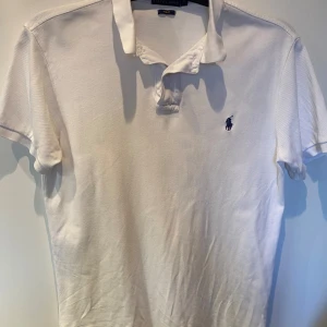 Vit pikétröja från Ralph Lauren - Säljer en klassisk vit pikétröja från Ralph Lauren i slim fit. Tröjan har korta ärmar och den ikoniska loggan broderad på bröstet. Perfekt för en stilren look. Storlek M, fits S. Mycket bra skick, förutom en minimal fläck på baksidan, går nog bort i tvätt! 