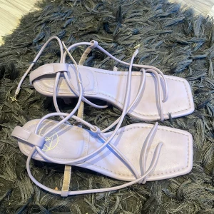 Ljuslila klackskor med snörning - Snygga ljuslila sandaler med snörning och fyrkantig tå. Perfekta för sommarens alla tillfällen. De har en elegant design med tunna remmar som knyts runt vristen.