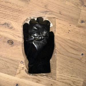 Svarta touch funktion handskar pekskärmsfunktion  - Säljer ett par svarta stickade handskar. Perfekta för att hålla händerna varma under kyliga dagar. De är förpackade i plast och ser ut att vara bekväma och praktiska för daglig användning.Stickade pekskärmshandskar: ledande tyg på tummen, pekfingrar och långfinger ger enkel åtkomst till dina smarta enheter utan att ta av handskarna i kallt väder.