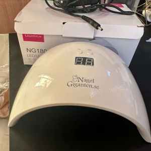 UV/LED lampa NG180 från Nagelgiganten - UV/LED lampa NG180 designad för härdning av UV och LED geléer. Utrustad med 18 LED dioder och timerinställningar på 30s och 60s. Automatisk avstängning efter 100 sekunder. Maximal strömförbrukning är 36W och den har en ingångsspänning på DC12V/1.5A.
