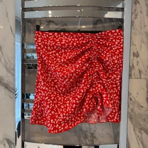 Röd blommig kjol - Säljer en röd blommig kjol i storlek S. Man kan knyta och välja längden själv på framsidan. Kjolen har även dragkedja på sidan. Köparen står för frakten!❤️