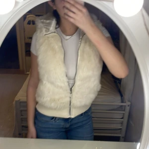Pälsväst  - Säljer en mysig vit pälsväst med dragkedja. Perfekt för att hålla sig varm och stilren under kyligare dagar. Västen har en bekväm passform och är lätt att matcha med olika outfits.