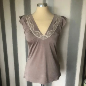  blus med spets från Saint Tropez - Supersöt  blus från Saint Tropez med v-ringning och broderad spetsdetalj längs halsringningen. Ärmlös modell med små volangdetaljer på axlarna. Sval och mjuk känsla, perfekt för vår och sommar. storlek M men bäst på S/M