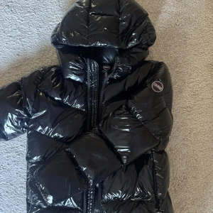Svart glansig dunjacka från Colmar - PRIS GÅR ATT DISKUTERA!                                                   Säljer en svart glansig dunjacka med huva från Colmar.     Storlek: Xs/S.  Dragkedja finns framtill och på sidan om den finns två fickor med dragkedja. Märkets logga sitter på en gummipatch och den är placerad på ena ärmen. Vadderingen består av 90% dun och 10% fjäder. Quiltad design som ger extra volym och värme. Använd ett fåtal gånger under vinter därav är den nästan som ny. 