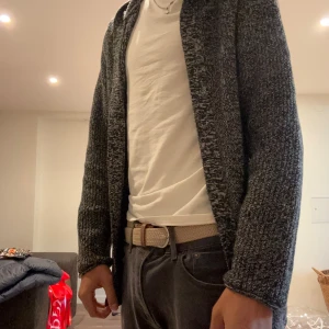 Mörkgrå stickad kofta - Säljer en mörkgråmelerad stickad kofta med öppen front. Koftan har lång ärm och en avslappnad passform, perfekt att slänga på sig över en t-shirt. Materialet är mjukt och ger en chill vibe till outfiten.