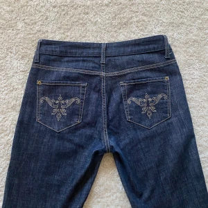 Mörkblå jeans med broderade bakfickor - Snygga mörkblå jeans från Lindex i klassisk modell med raka ben och broderade detaljer på bakfickorna. Jeansen är lågmidjade, har fem fickor och gylf med knapp. Perfekta till vardags för en stilren look. midjemåttet är 40 cm och innerbenslängden 78cm, jag är 168cm på bilden✨✨