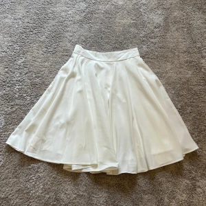 Vit flowy långkjol med dragkedja - Säljer en vit långkjol med mjukt, flowy tyg och diskret dragkedja bak. Kjolen har ett tunt foder och sitter snyggt i midjan. Perfekt för dig som gillar en klassisk och clean stil med lite extra volym i kjolen.