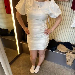 Vit kort klänning med puffärm - Supersnygg vit kort klänning med puffiga kortärmar och tight passform. Klänningen har rynkade detaljer längs sidorna som ger jättefin form🤩 passar bra till allt, student sommarfirande osv! Endast använd en gång som studentklänning, så väldigt bra skick