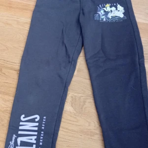 Disney Villains svarta mjukisbyxor - Svarta mjukisbyxor från Disney med tryck av Disney Villains och texten 'Happily Never After' på benet. Byxorna har resår i midjan och är gjorda i mjukt material, perfekta för chill dagar. Motiv med klassiska skurkar från Disney på ena benet.