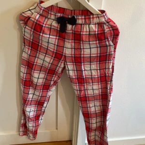 Röd-rutiga mjukisbyxor från Kappahl - Supermysiga mjukisbyxor från Kappahl i röd, vit och blå rutig bomull. Byxorna har resår i midjan med en mörkblå rosett framtill och avslappnad passform. Perfekta för chill dagar hemma eller som pyjamasbyxor.
