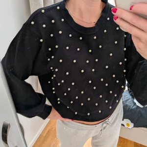 Svart tröja med pärldetaljer - Svart långärmad tröja med coola pärlor över hela framsidan. Tröjan har en croppad passform och är gjord i ett mjukt stickat material. Perfekt för dig som vill sticka ut lite extra med snygga detaljer.