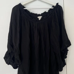 Svart blus från H&M - Säljer en svart blus från H&M i storlek 42. Blusen har en offshoulder-modell med resår och volangdetaljer vid halsringningen och ärmsluten. Den är lätt och tunn, men inte genomskinlig! 