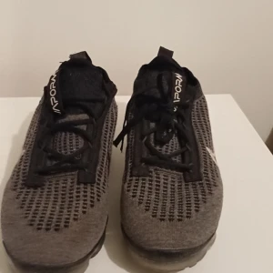 Nike Vapormax Flyknit sneakers grå - Nike Vapormax Flyknit sneakers i grå och svart med transparent sula. Ovandelen är stickad med mesh för extra ventilation och har snörning framtill. Swoosh-logga i vitt på sidan och VAPORMAX-etikett på plösen. Perfekt för dig som gillar sportig stil. Pris kan diskuteras!!