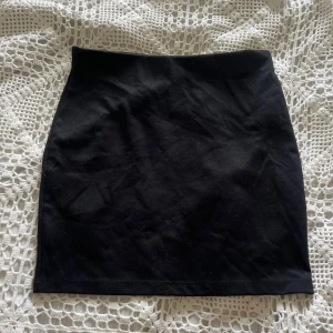 Svart kortkjol   - En stilren svart kortkjol från C i storlek S. Kjolen har en rak och tight passform med enkel design utan detaljer eller mönster. Materialet känns mjukt och stretchigt, perfekt för dig som gillar minimalistisk stil.