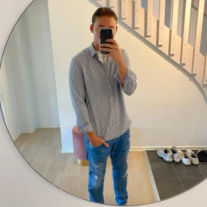 Blårutig skjorta från Riley - Snygg skjorta från Riley i klassiskt blårutigt mönster. Skjortan har lång ärm, vit-blå färgton och knappar framtill. Materialet är mjuk bomull som känns skönt mot huden. Perfekt till jeans och sneakers för en chill look. OBS! En liten skada framtill, men ingenting man lägger märke till. Den saknar även en knapp på höger arm.