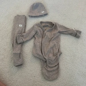 Baby body  - Supersöt ribbad omlottbody i beige från H&M, perfekt för de minsta. Setet inkluderar matchande byxor och mössa. Bodyn har tryckknappar och långa ärmar, tillverkad i mjuk bomull för extra komfort.