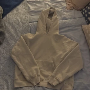 Beige hoodie med huva och magficka - Snygg beige hoodie med klassisk huva och stor magficka framtill. Tröjan har ribbade muddar vid ärmslut och nederkant, perfekt för en chill och avslappnad stil. Passformen är loose och materialet känns mjukt och skönt mot huden. Är ifrån gina tricot.