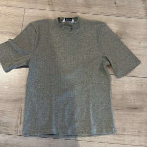 Glittrig grå t-shirt från Kappahl - Snygg grå t-shirt från Kappahl i storlek L med glittriga detaljer. T-shirten har korta ärmar, ribbad struktur och en lite högre halsringning. Perfekt för dig som vill sticka ut lite extra med en enkel men cool look.