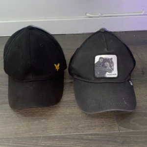 Svarta kepsar Lyle & Scott och Goorin Bros - Två svarta kepsar säljes! Ena är från Lyle & Scott med gul logga framtill, klassisk böjd skärm och justerbar rem. Den andra är en Goorin Bros truckerkeps med mesh baktill, broderad patch med pantermotiv och snapback. Perfekt för dig som gillar stilrena accessoarer.