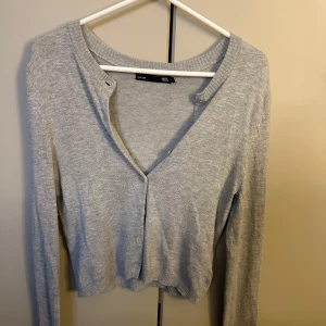 Grå kofta från 157, XS - Ljusgrå croppad kofta från 157 i storlek XS, känns som xxs så den är kort och tajt. Långa ärmar och knappar framtill. Tillverkad i mjukt stickat material, perfekt för lager-på-lager och chill vibes. Enkel och stilren design som funkar till många outfits.