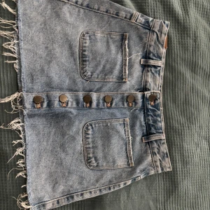 Blå jeanskjol från Zara Trafaluc - Snygg blå jeanskjol från Zara Trafaluc med råa kanter, stora fickor fram och bak samt knappar längs hela framsidan. Klassisk denimlook som är lätt att styla med allt. Perfekt för dig som gillar en avslappnad vibe.