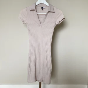 Beige ribbad kortklänning med krage - Supersnygg beige kortklänning från H&M med ribbad struktur och v-ringad hals med krage. Klänningen har korta ärmar och sitter figurnära, perfekt för dig som gillar enkel men trendig stil. Passar dig som vill ha en clean och fräsch look.