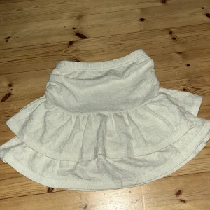 Vit volangkjol med shorts under - Supersöt vit kortkjol med volanger och inbyggda shorts under. Kjolen har en lätt struktur i tyget och är perfekt för dig som vill ha en luftig och bekväm stil. Passar perfekt till sneakers och en enkel topp för en fräsch look.