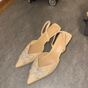 Beige pumps med strassfjäril - Snygga beige pumps från H&M med spetsig tå och låg klack.  Storlek 38 , testad en gång 