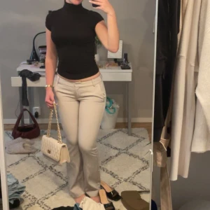 Beige bootcut kostymbyxor från Bik Bok - Snygga beige kostymbyxor från Bik Bok med bootcut passform och lowwaist. Byxorna har klassisk design med fickor fram och bälteshällor. Perfekta att styla med en tight topp eller oversized skjorta för en clean look. Jag är 1.70 och längden är perfekt. 