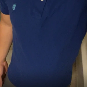 Blå pikétröja från U.S. Polo Assn - Snygg blå pikétröja från U.S. Polo Assn med klassisk krage och två knappar framtill. Tröjan har broderad logga på bröstet och är gjord i mjuk bomull. Perfekt till jeans eller shorts för en chill look. Fick den i julklapp nåt år sedan men har aldrig använt den!