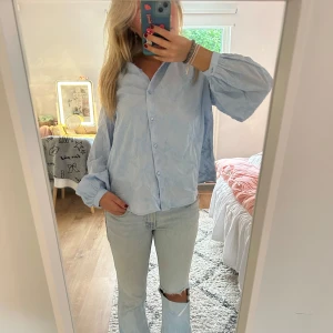 Ljusblå broderad blus - Säljer en ljusblå skjorta med broderade detaljer och knappar framtill. Skjortan har en loose passform och ballongärmar med knapp vid ärmslut. Perfekt för dig som gillar en chill och trendig look.