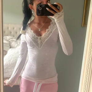 Vit intimissimi spets tröja - Supersöt vit långärmad blus med djup v-ringning och fina spetsdetaljer vid halsringning och ärmslut. Sitter tight och har en feminin, romantisk vibe. Perfekt att styla med jeans eller kjol för en trendig look.
