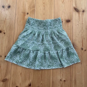 Grön blommig volangkjol Gina Tricot XS - Supersöt grön kortkjol från Gina Tricot i storlek XS. Kjolen har små vita blommor, bred smock i midjan och volang nertill. Perfekt för vår och sommar, lätt och luftig känsla. Kan användas som både topp och kjol