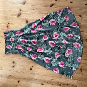 Blommig långkjol - Supersnygg långklänning med tropiskt blommönster i rosa, vitt och grönt på mörk botten. Smockad upptill för en bekväm passform och flowy kjol. Perfekt för sommarens alla äventyr! Man kan använda både som kjol och klänning